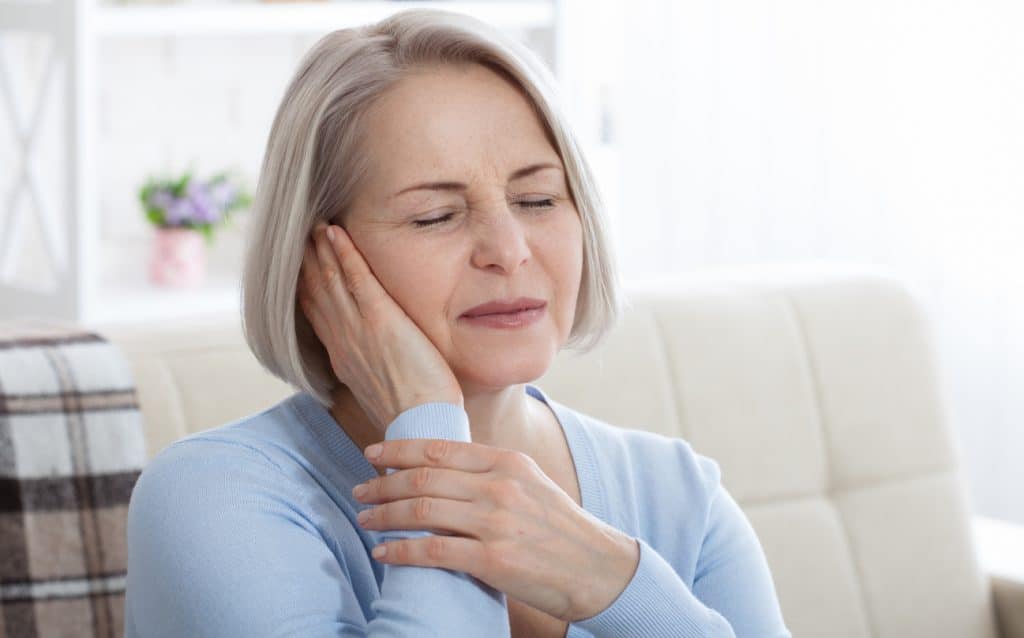 Une femme grimaçant et tenant son oreille de douleur.